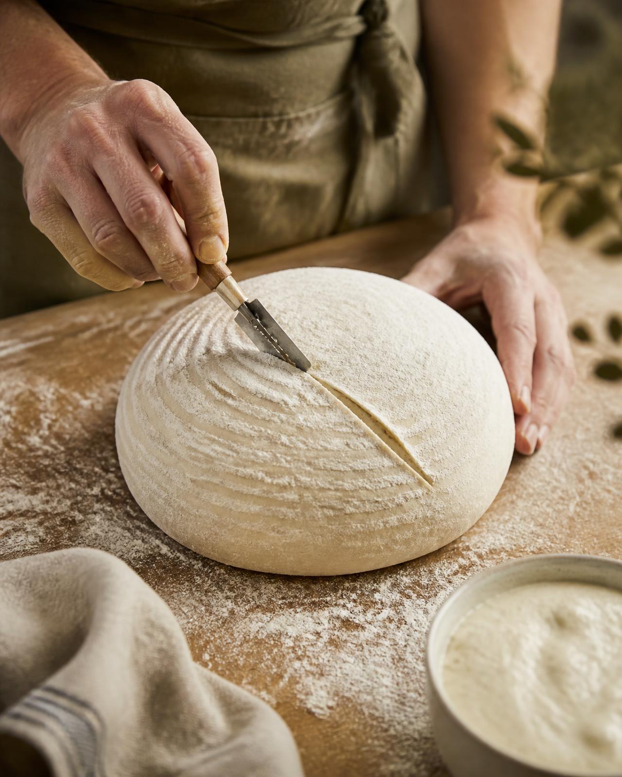 Debbie Garcia scoring a naturally fermented sourdough loaf on a flour-dusted work surface